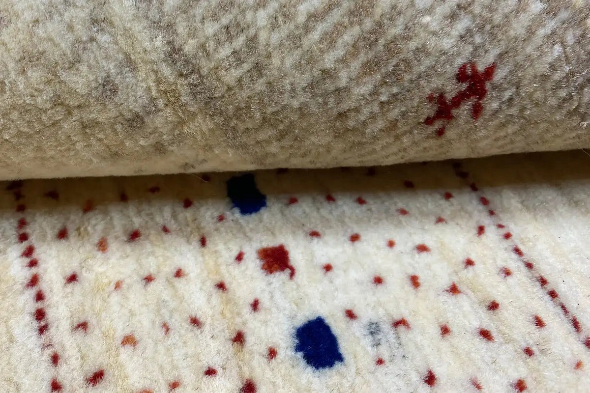 Gabbeh rug detail: beige pile with colorful patterns and small red/blue dots