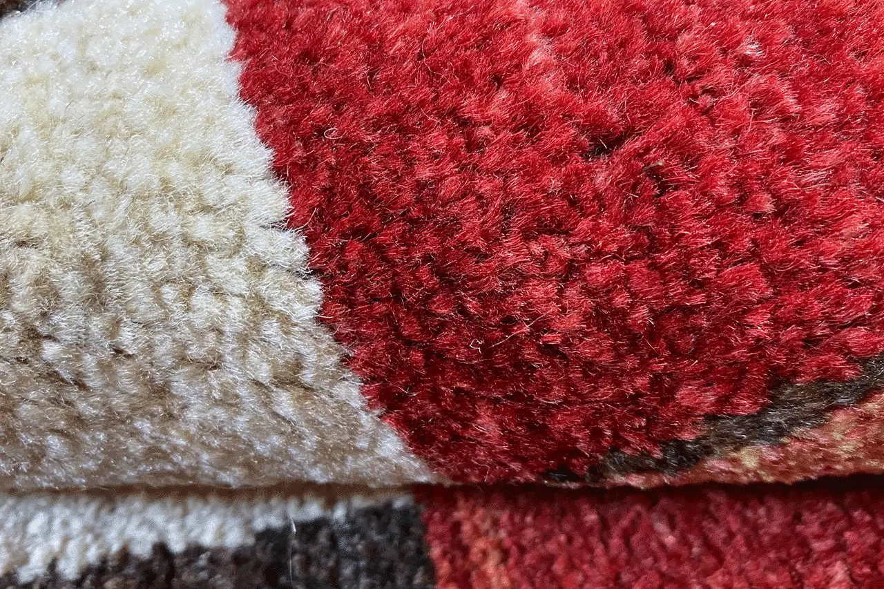 Gabbeh rug detail: red and beige wool with a multicolored border