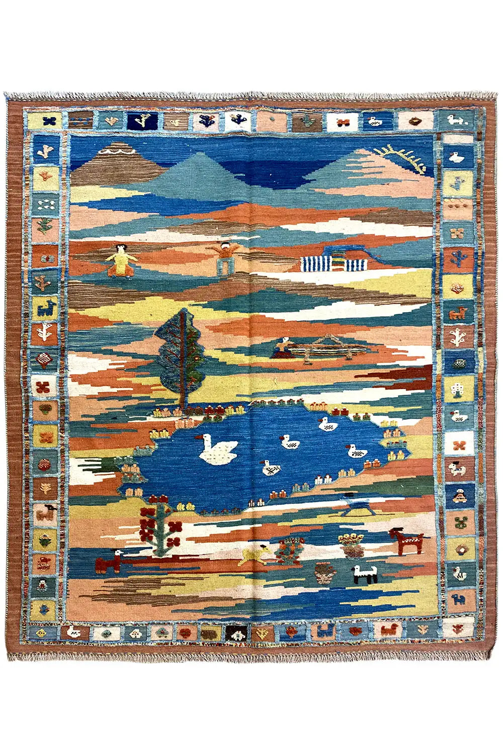 Kilim rug with a landscape motif in blue, beige, and orange, with a fringed border
