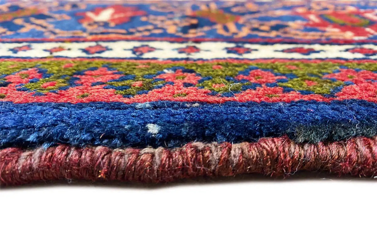 View of the carpet edge: blue pile with a red accent and a fringed side border