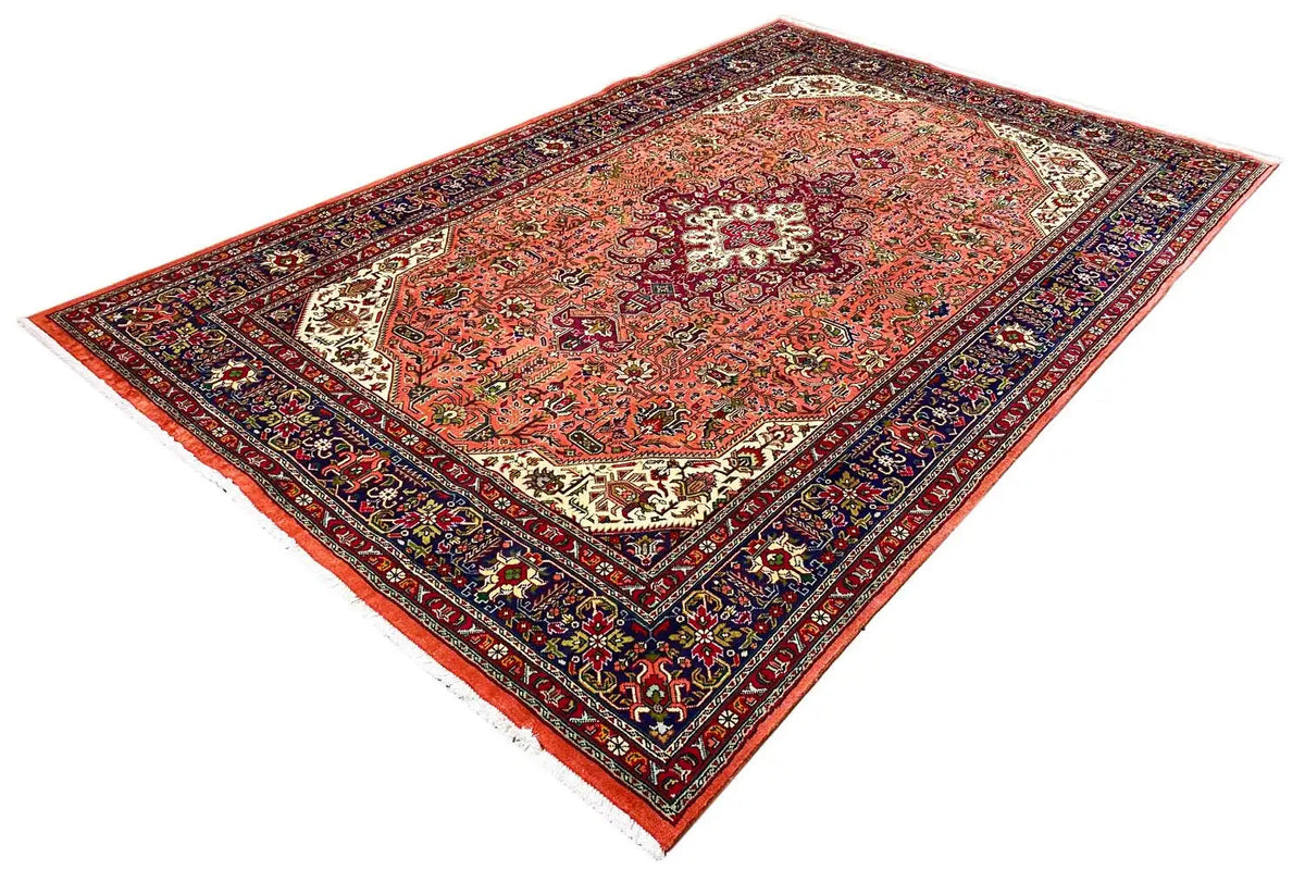 Corner view of a Tabriz rug: red-orange patterned field with a dark blue decorative border