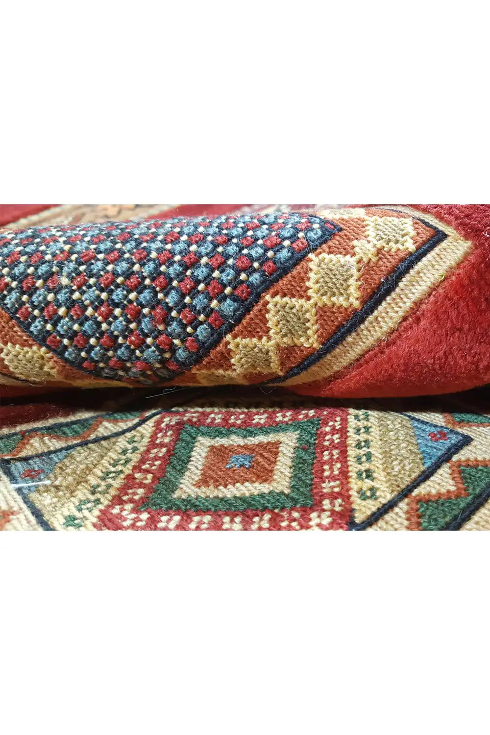 Folded carpet view with a blue and red diamond pattern, beige accents, and fringes
