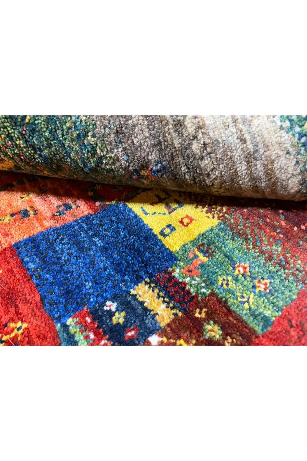 Gabbeh rug with folded edge: colorful patterns on a gray backing.