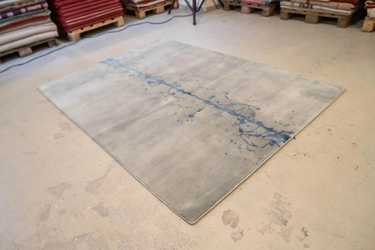 Rug 153x209 cm in workshop view, gray surface with a blue ink streak.