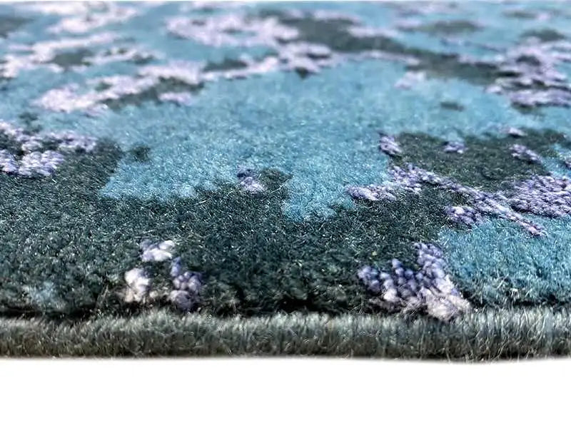 Close-up: dense carpet pile with a blue-green texture and delicate pattern.
