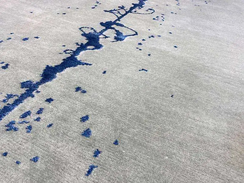 Close-up: gray carpet with blue ink stains, splatters, and a linear pattern.