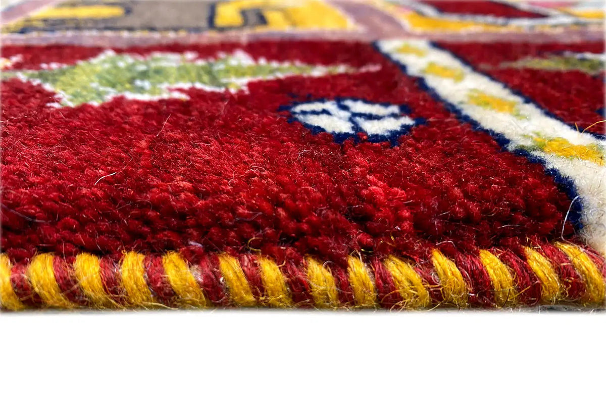 Close-up: red Gabbeh Lori rug with a fluffy pile, multicolored border, and fringes