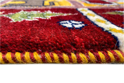 Close-up: red Gabbeh Lori rug with a fluffy pile, multicolored border, and fringes