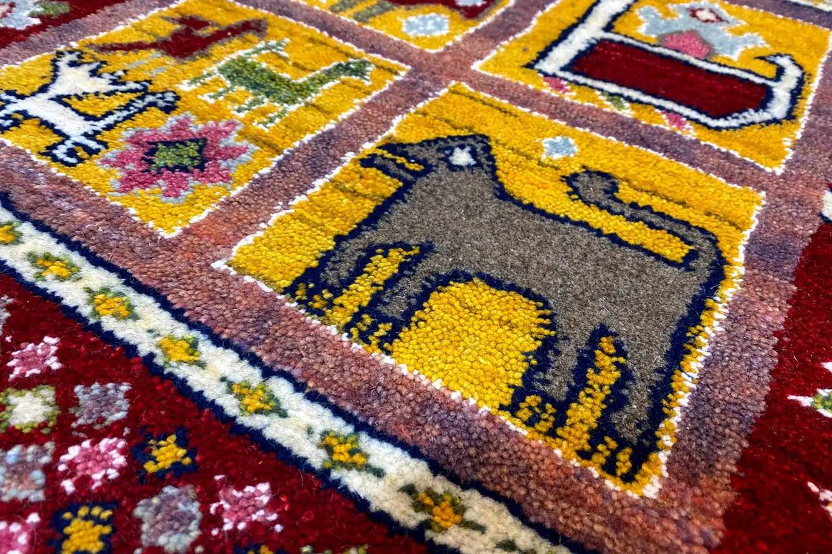 Gabbeh Lori rug close-up: yellow symbols in the border on a red background