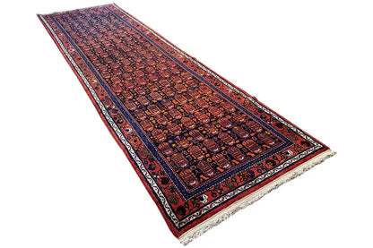 Hamadan rug in angled view: red-and-blue pattern with a dark blue border line and fringes