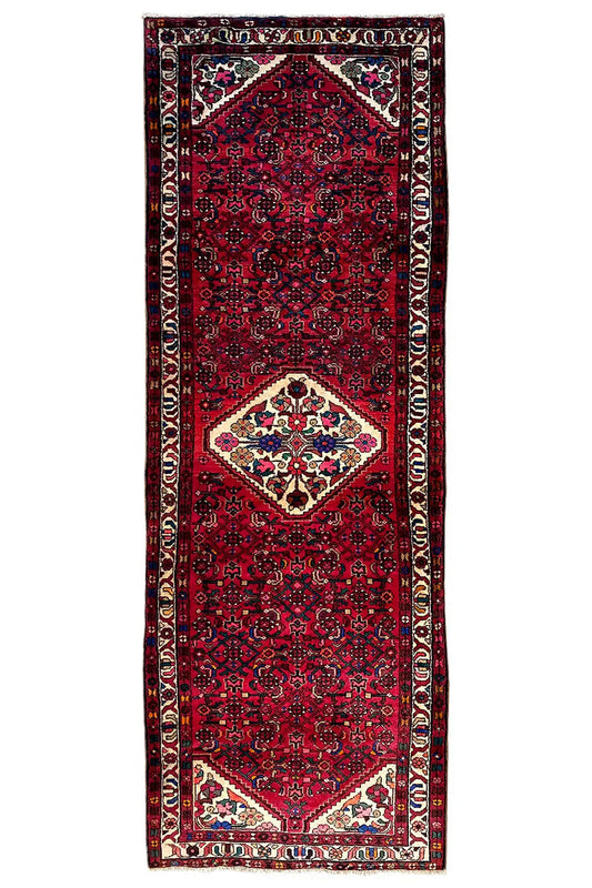 Hamadan runner in a still image: red field pattern, white medallion, multicolored border trim