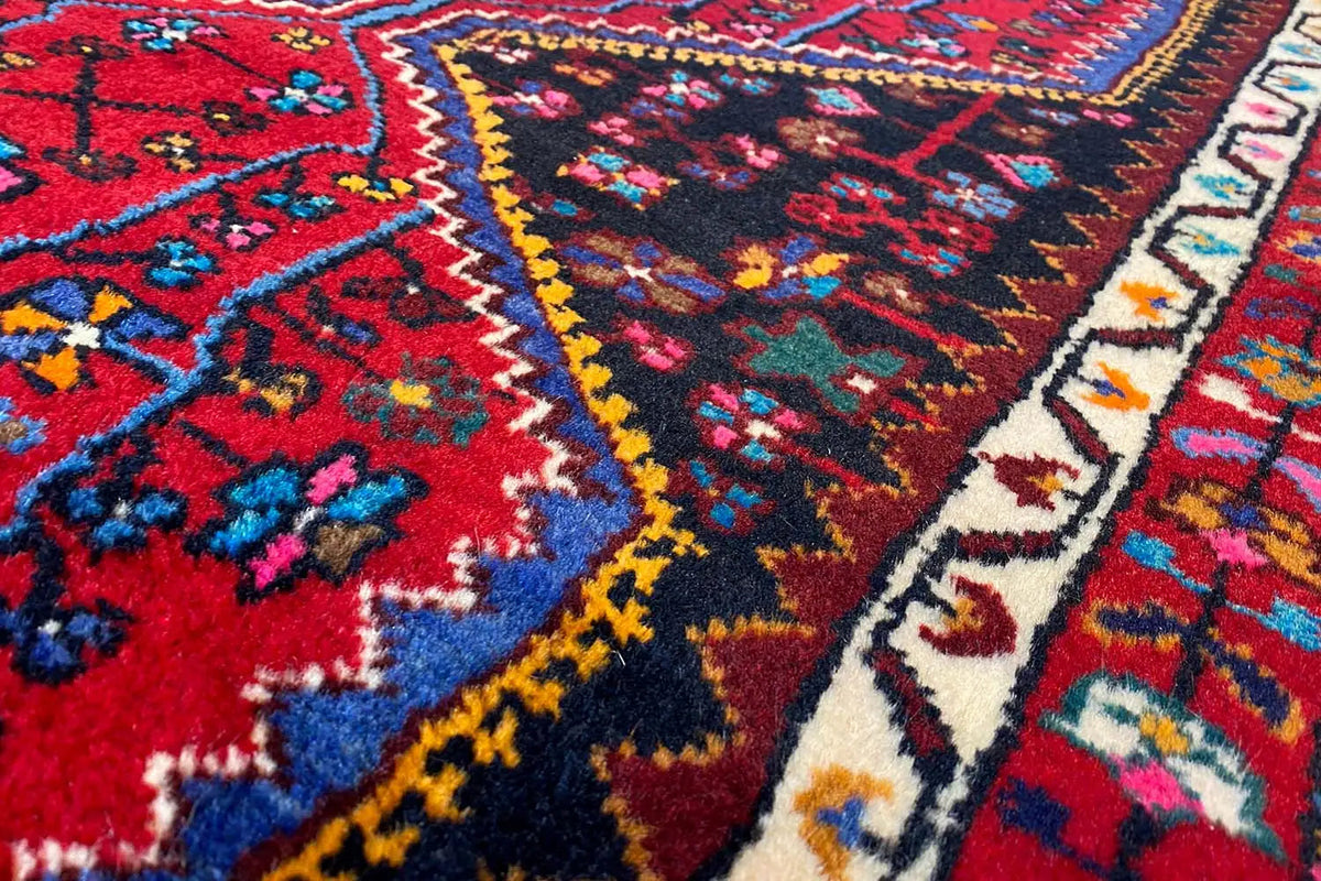Hamadan rug texture close-up, dense pile with colorful decorative motifs and fringed edge