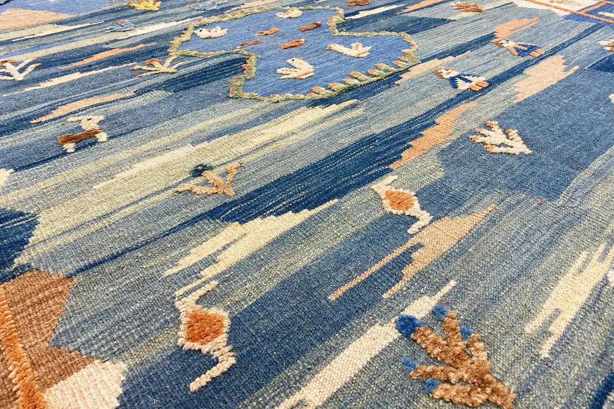 Detailed view: blue-and-beige kilim with stylized figures and decorative stitching