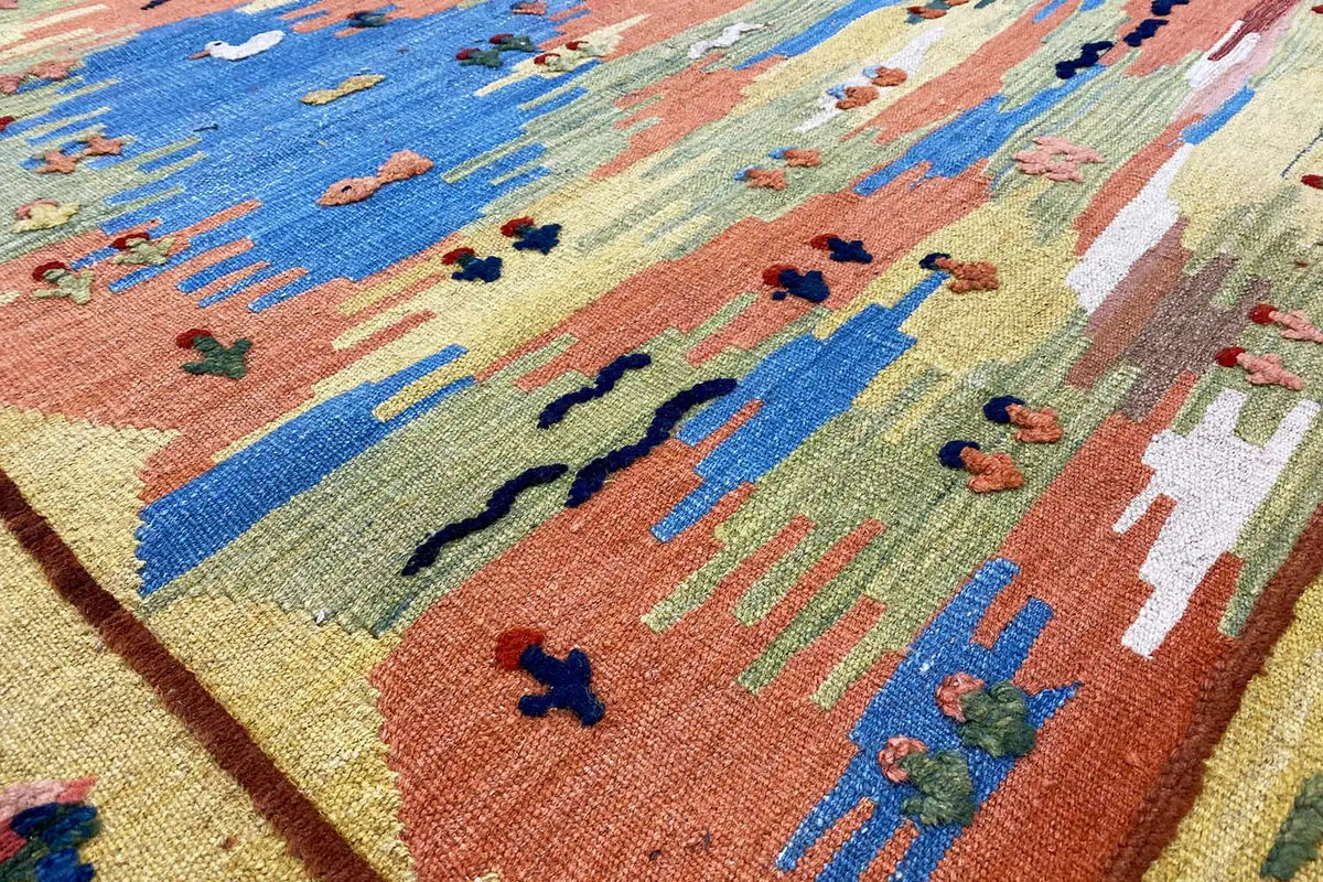 Close-up of a kilim rug with colorful figures and landscape elements