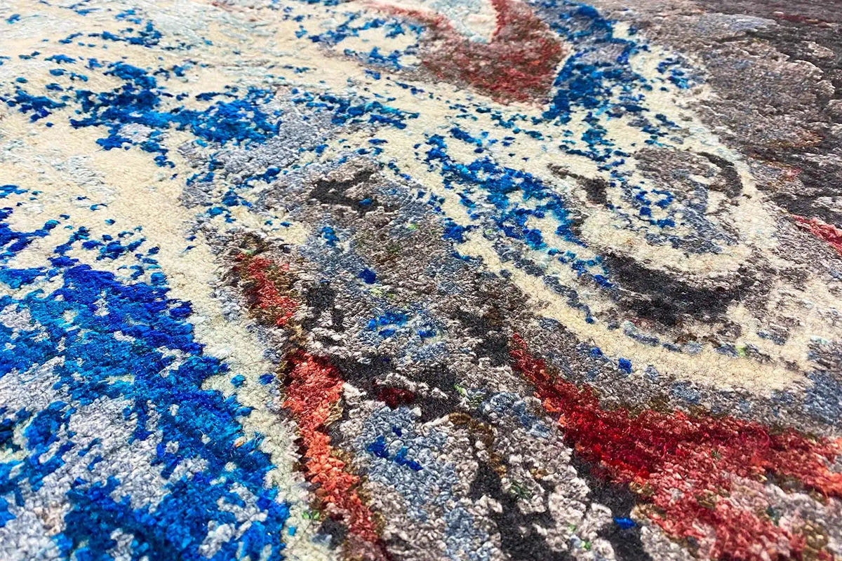 Designer rug with an abstract pattern in blue, gray, and red, textured surface.