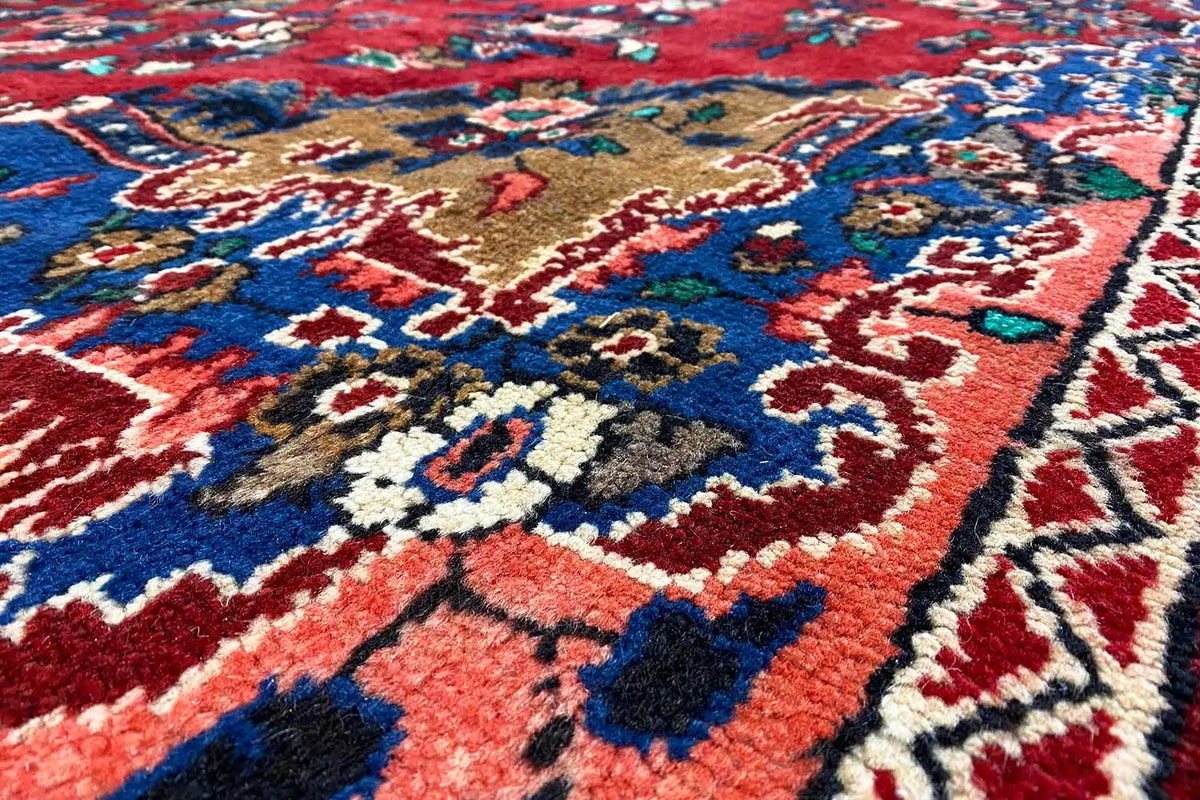 Oriental rug with a red background and blue-and-gold ornaments, close-up detail of the border