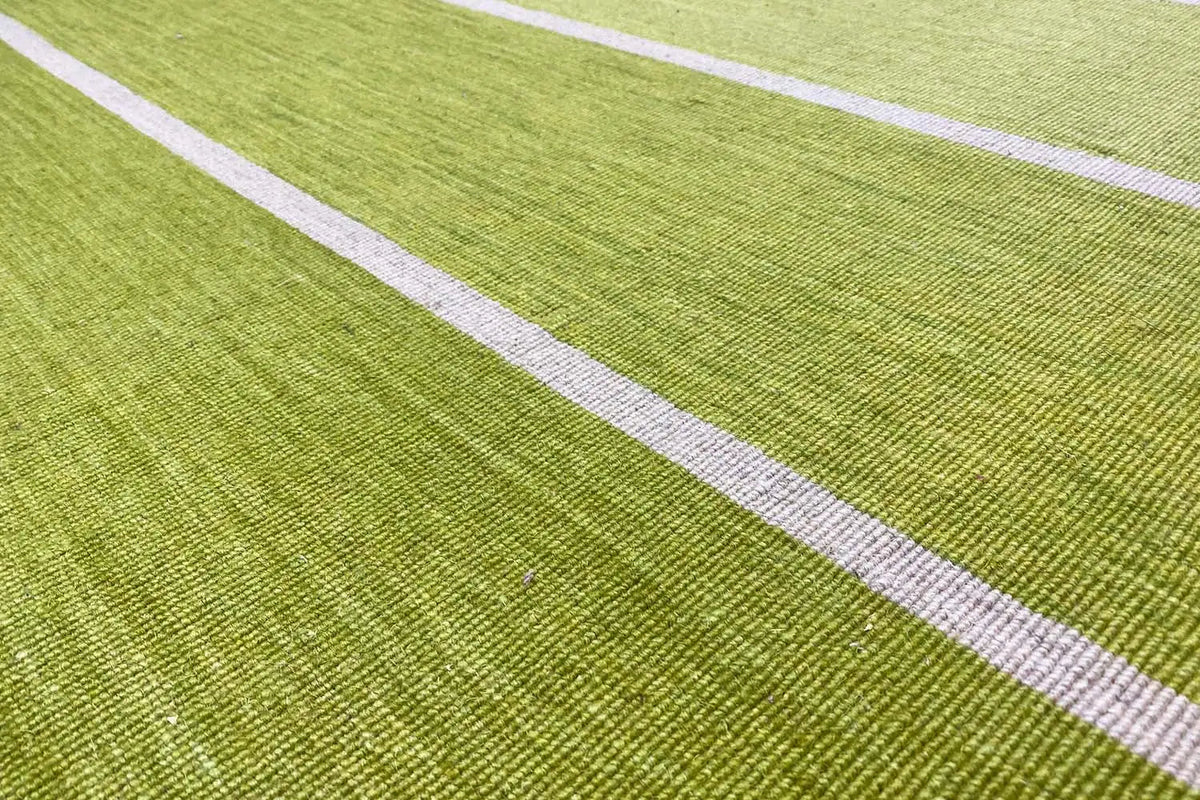 Close-up of a kilim rug: green surface with white longitudinal stripes and a fine woven texture