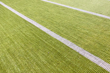 Close-up of a kilim rug: green surface with white longitudinal stripes and a fine woven texture