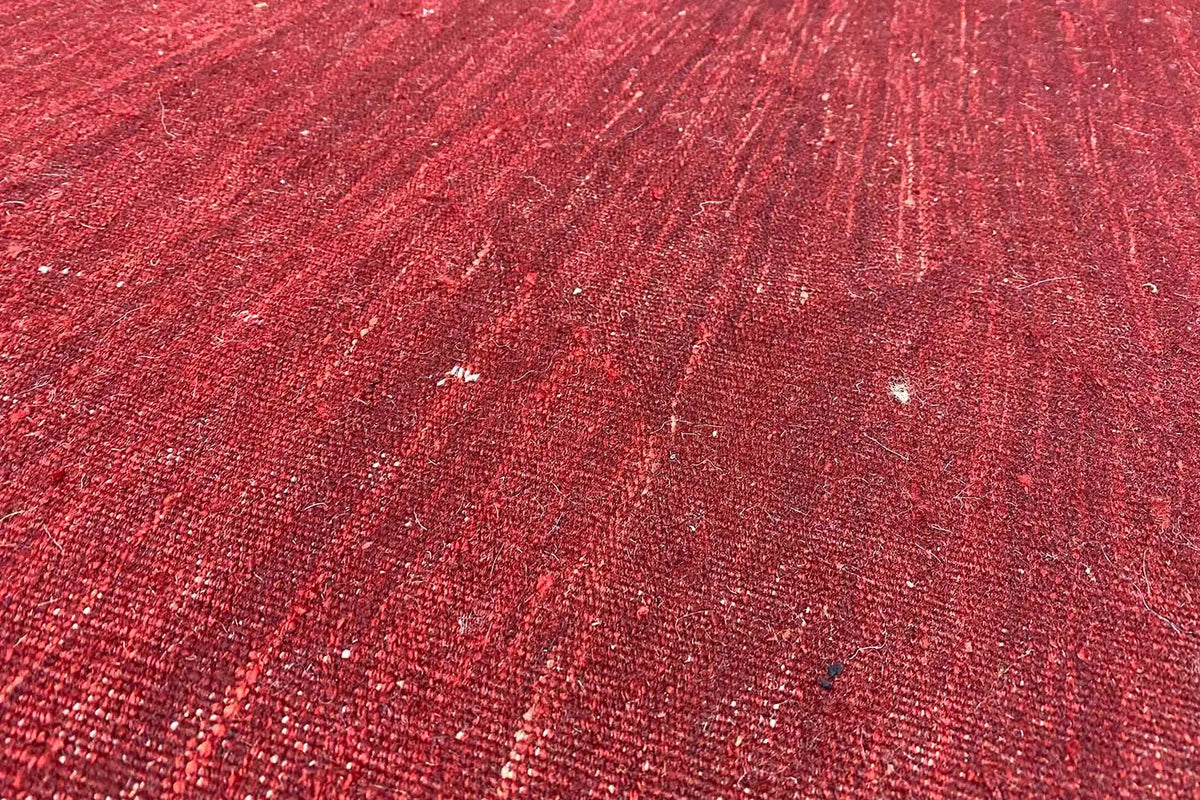 Close-up of the surface of a red kilim rug with shimmering fibers and subtle patterning