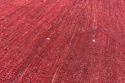 Close-up of the surface of a red kilim rug with shimmering fibers and subtle patterning