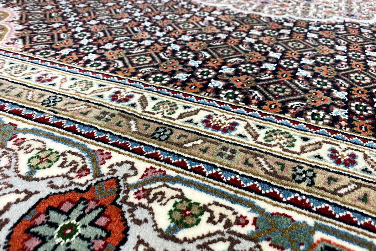 Tabriz-style rug with a multicolored ornamental and border pattern, close-up