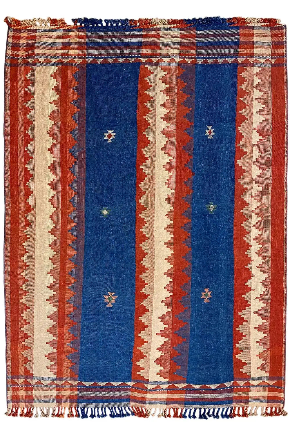 Rug with vertical stripes in rust red, blue, and cream, with fringes all around