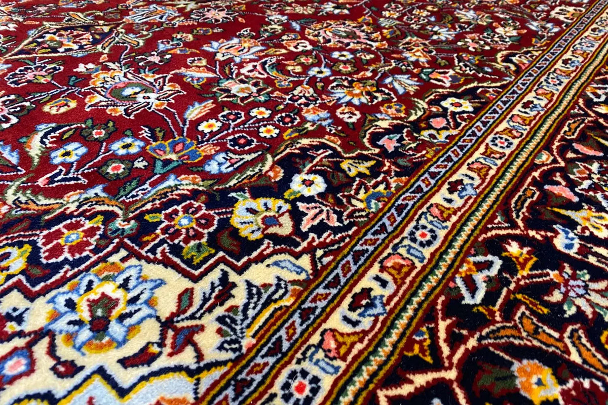 Close-up of a Keshan rug: colorful floral patterns in blue, red, and green along the edge.