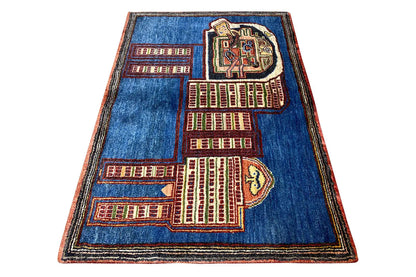 Blue Gabbeh rug spread at an angle with a red and beige city and lion pattern