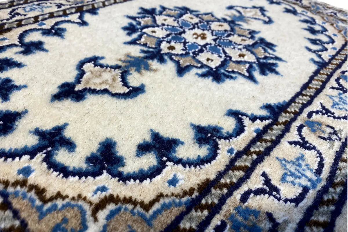 Close-up: white and blue Nain rug with a blue ornament and fringes along the edge