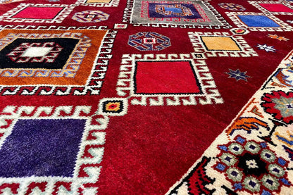 Carpet detail with a red background and geometric shapes in blue, purple, and beige