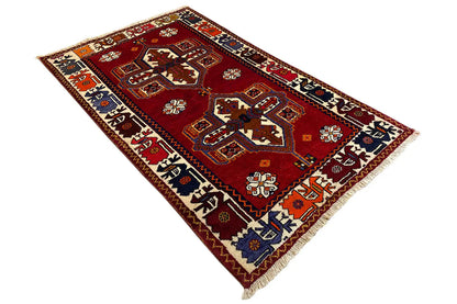 Rectangular red rug with Shiraz-Qashqai motifs and fringes along the edges