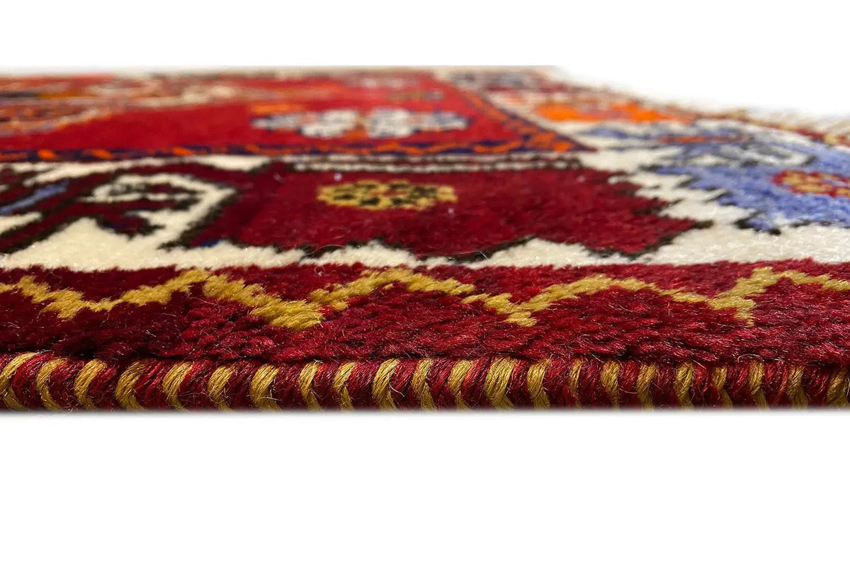 Close-up: red woven carpet with a multicolored border and fringes along the edge
