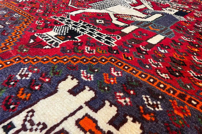 Close-up: red carpet pattern with white animal and diamond motifs and a dark border