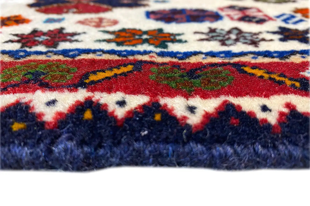 Close-up: carpet edge with fringes; cream-colored pile with blue-red stripes