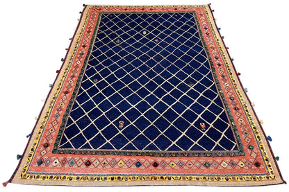 Large rug with a dark blue grid pattern, red border, and colorful tassels