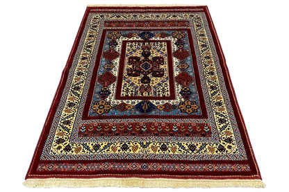 Rug viewed at an angle with a dark red border, blue center, and beige fringes