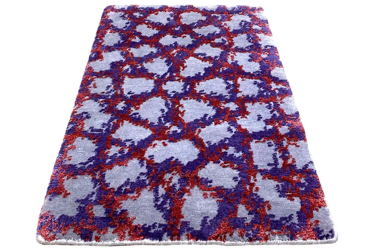 Rectangular rug with an abstract patchwork pattern in blue, red, and purple on a light background.