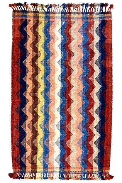 Vertically oriented rug with a zigzag pattern in red, blue, and cream, with fringes on all sides.