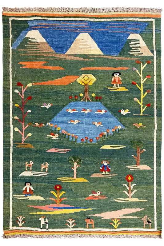 Green kilim rug with figures, trees, and mountains, a surrounding border and fringes