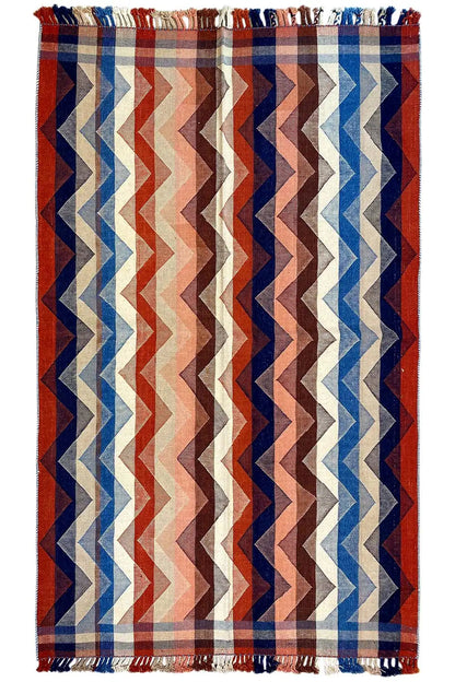 Rug with a zigzag pattern in red, blue, and beige, with fringes on both sides