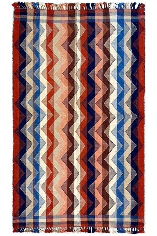 Rug with a zigzag pattern in red, blue, and beige, with fringes on both sides