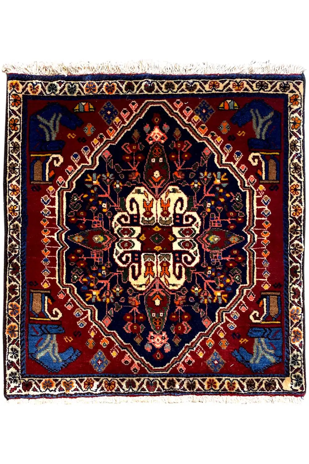 Square rug with a dark blue and red ornamental pattern and white fringes