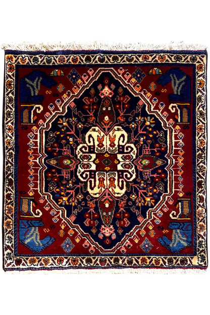 Square rug with a dark blue and red ornamental pattern and white fringes