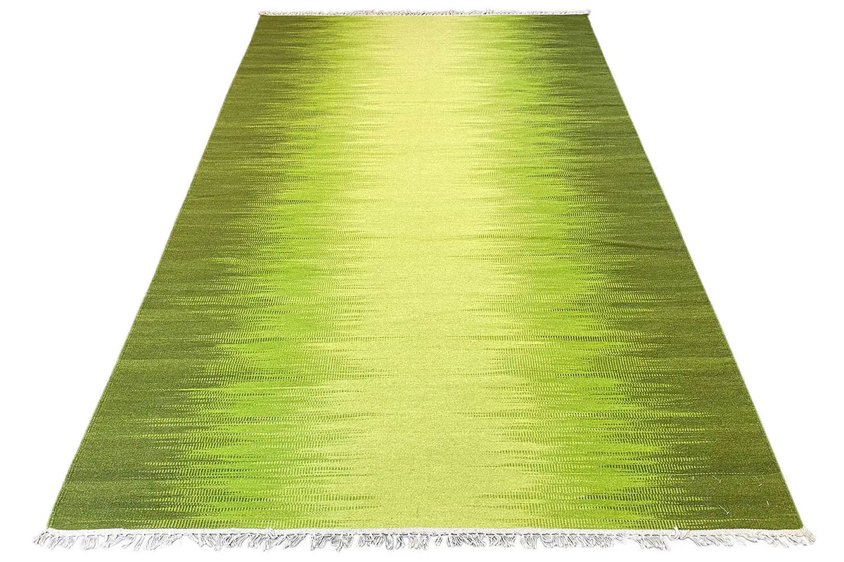 Green kilim rug in angled view with fringes along the bottom edge
