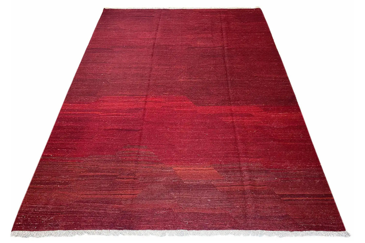 Red kilim rug in a trapezoidal shape with fine fringes and striped color gradients