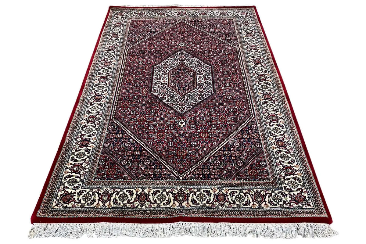 Rug in three-quarter view: red central field, greige border and fringes