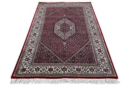 Rug in three-quarter view: red central field, greige border and fringes