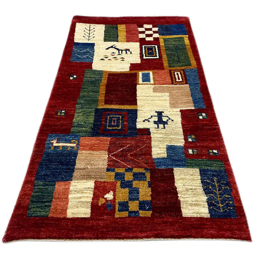Gabbeh rug with a geometric patchwork pattern in red, cream, blue, and green.
