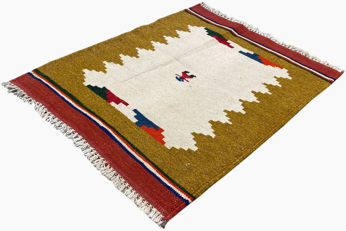 Kilim rug spread diagonally: ochre, white patterned field, red border, and fringe