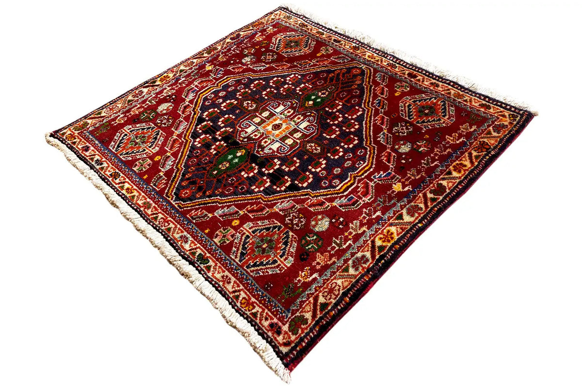 Square rug with a traditional ornamental pattern in shades of red and green, fringes